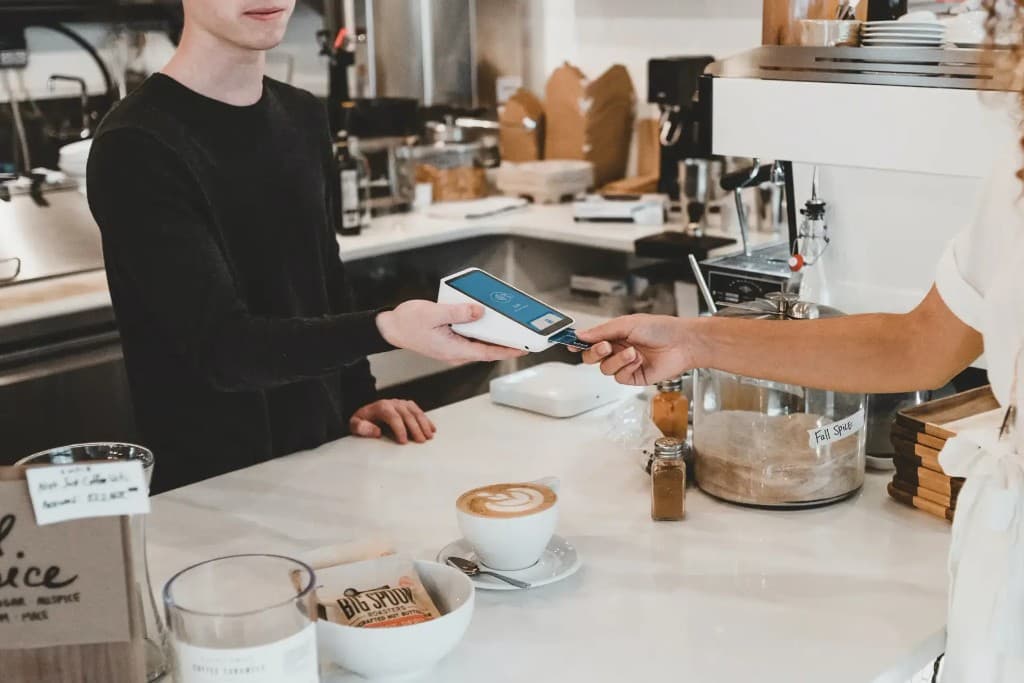 Un employé de café tend un terminal de paiement à un client qui insère sa carte, un latte sur le comptoir.